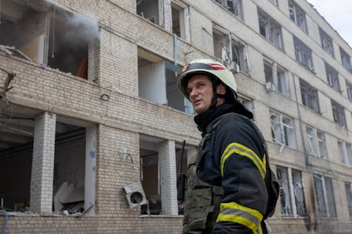 Free Firefighter in front of a Residential Building Destroyed by Shelling Stock Photo