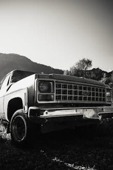 Black and white photo of an abandoned vintage pickup truck in a mountainous landscape.