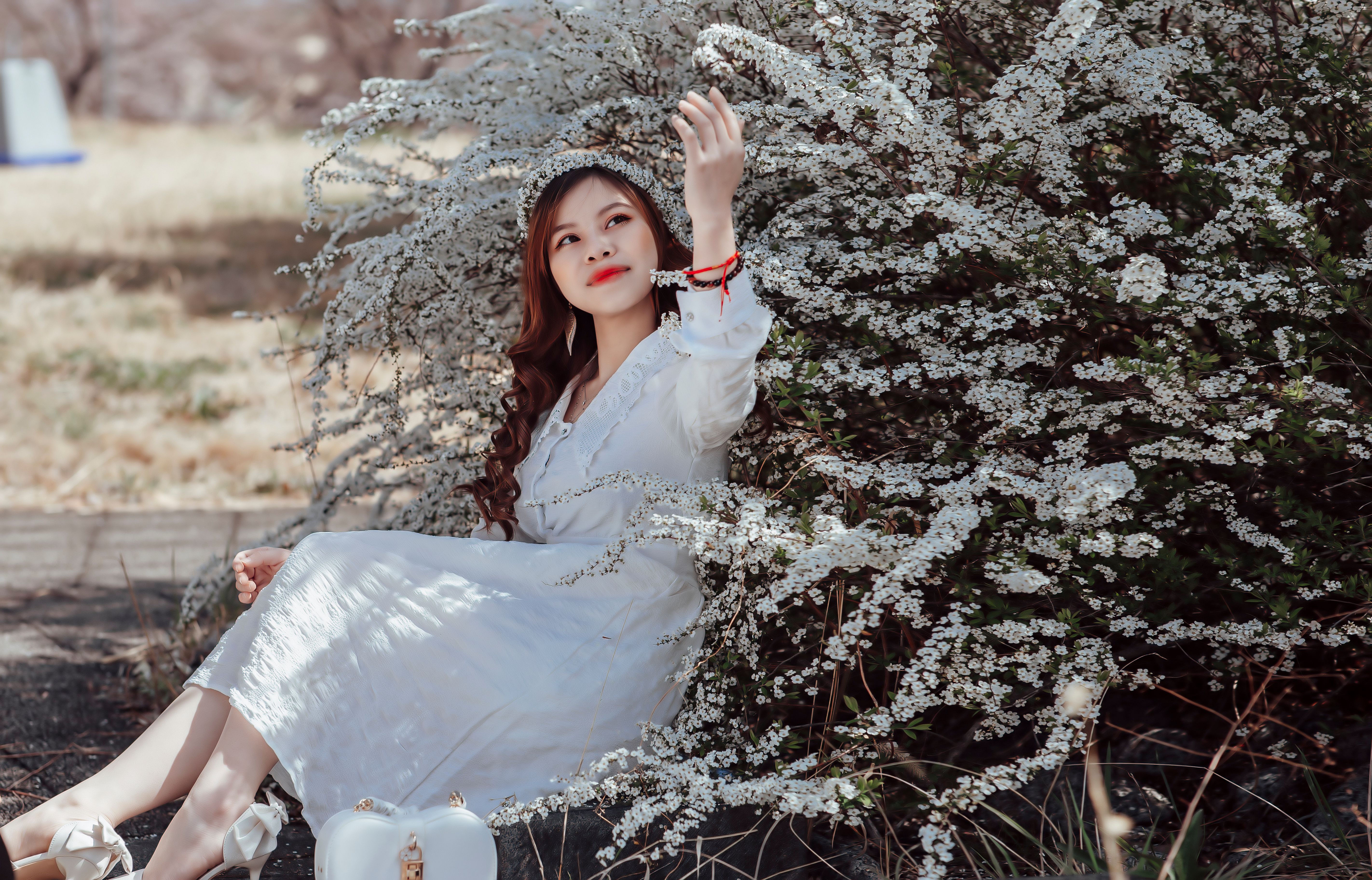 A young woman enjoys a peaceful moment amidst white blossoms in a park.