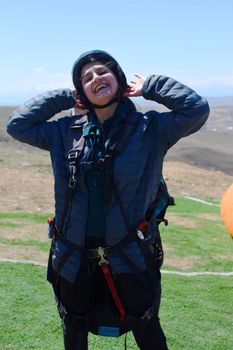 Happy woman paragliding outdoors, wearing helmet, arms raised in excitement.