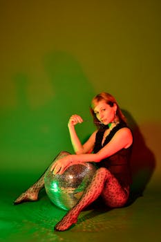Woman sitting on floor with a disco ball in a studio with green lighting.
