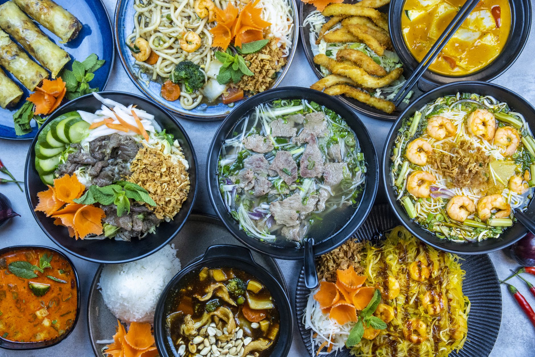 A vibrant assortment of Asian cuisine, showcasing soups, noodles, and spring rolls, garnished with fresh herbs.