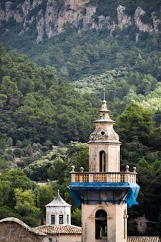 Bell tower set against lush green mountains with serene forest background.