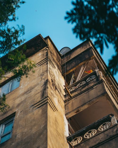 Free Aged concrete apartment building with balconies under a clear blue sky, viewed from below. Stock Photo