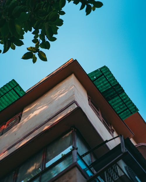 Free Low-angle view of a modern building with blue sky and leafy branch, creating an architectural contrast. Stock Photo
