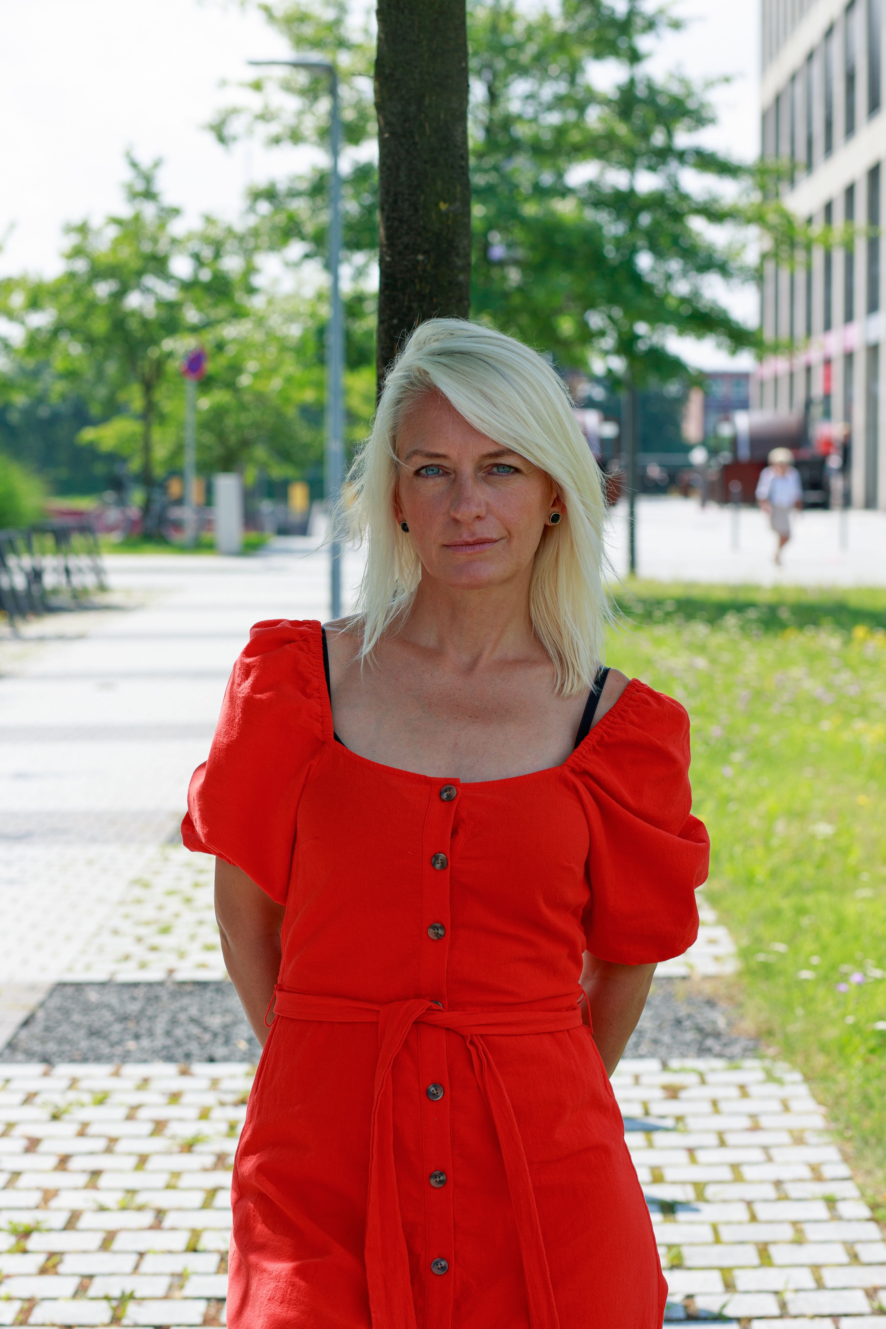 Senior woman with white hair smiling outdoors in a vibrant red dress.