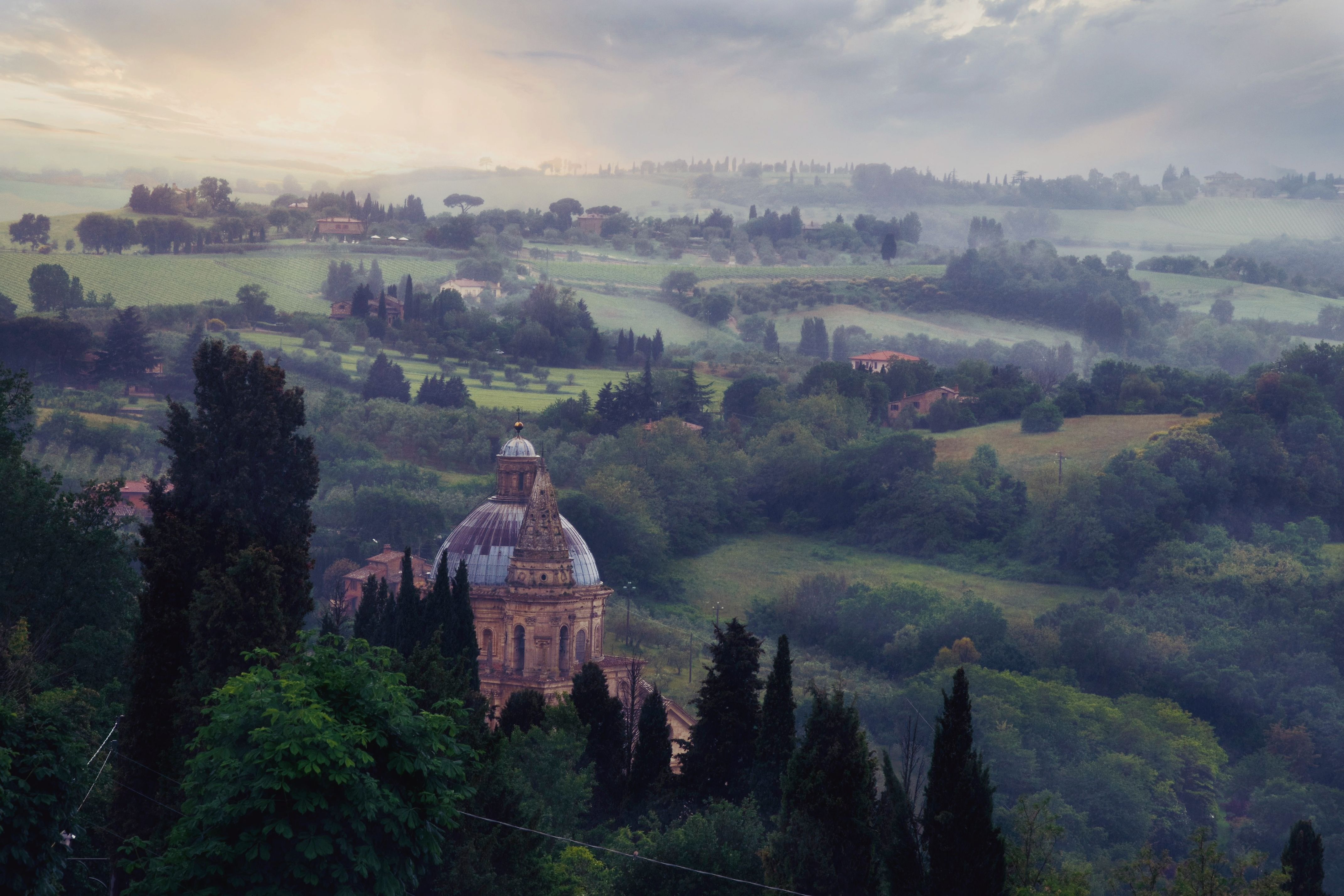 A serene misty landscape in Italy with greenery and historical architecture.