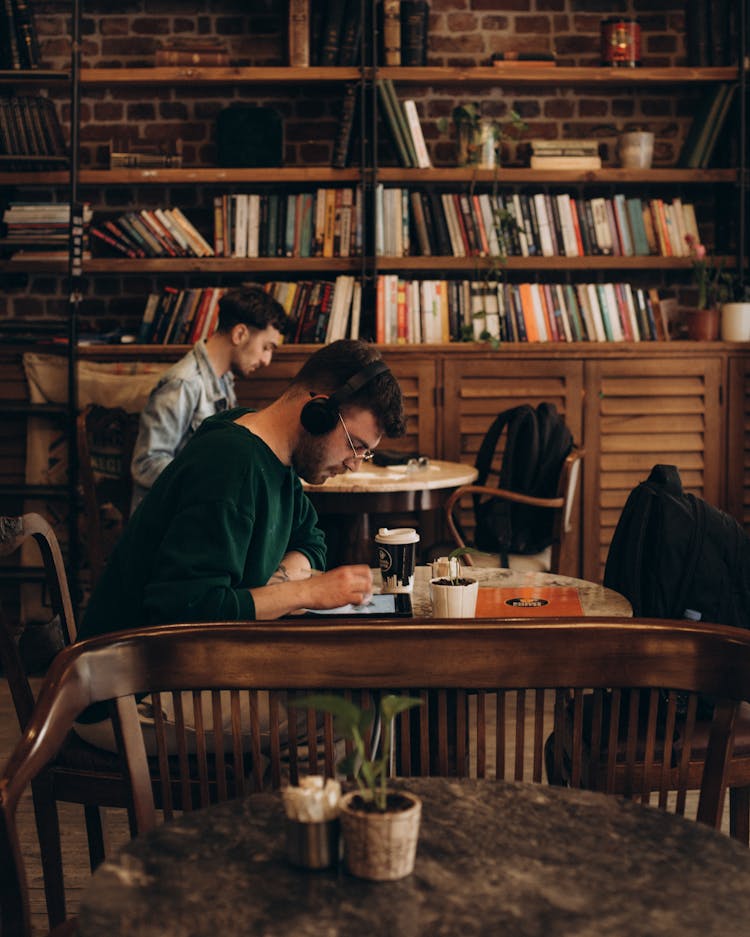 Students Sitting At Coffee Tables And Making Notes In Library