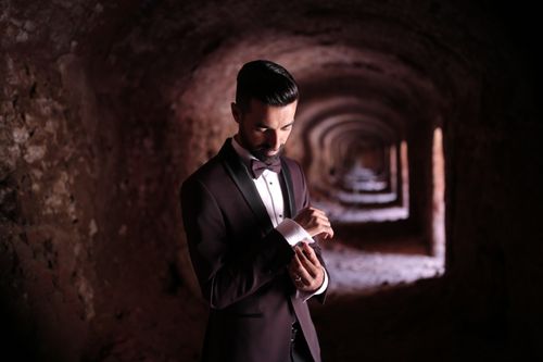 Free A man elegantly dressed in a suit adjusting cufflinks in a vintage tunnel. Stock Photo