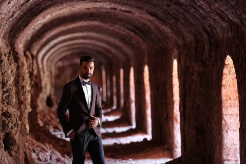 Free Fashionable man in a black suit posing in a brick tunnel, exuding confidence and style. Stock Photo