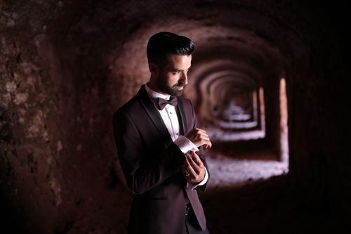 Free A fashionable man in a suit adjusts his cufflinks in an ancient tunnel setting, offering a formal yet stylish vibe. Stock Photo