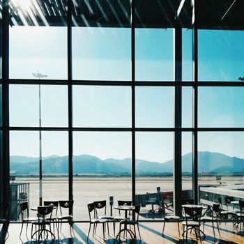 Empty airport lounge with a view of mountains through large glass windows at daytime.