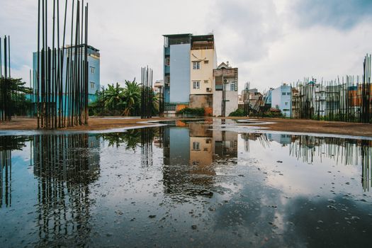 Reflection of urban buildings and construction rods in a puddle on a cloudy day.