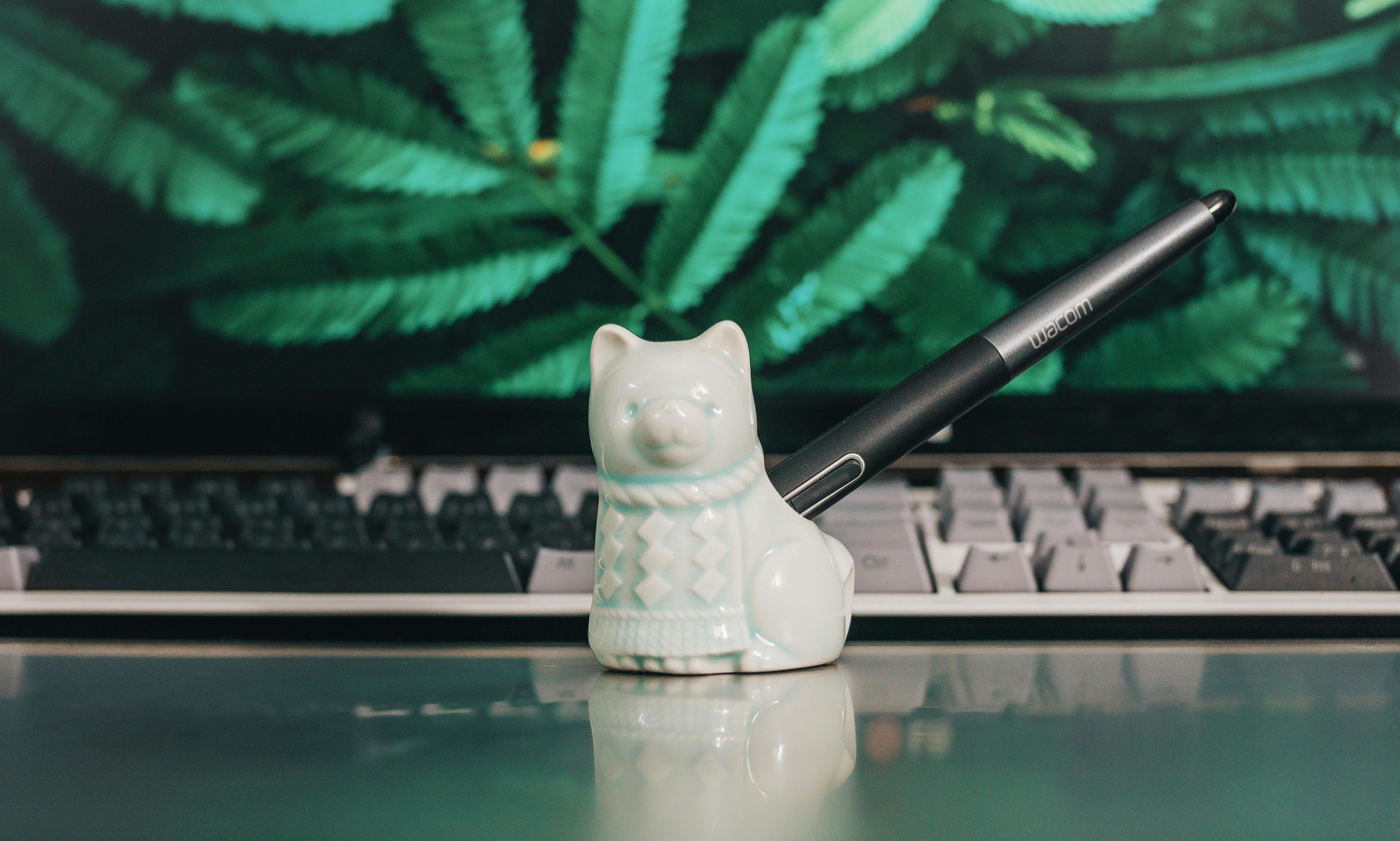 A ceramic cat pen holder placed on a desk in front of a keyboard and monitor.