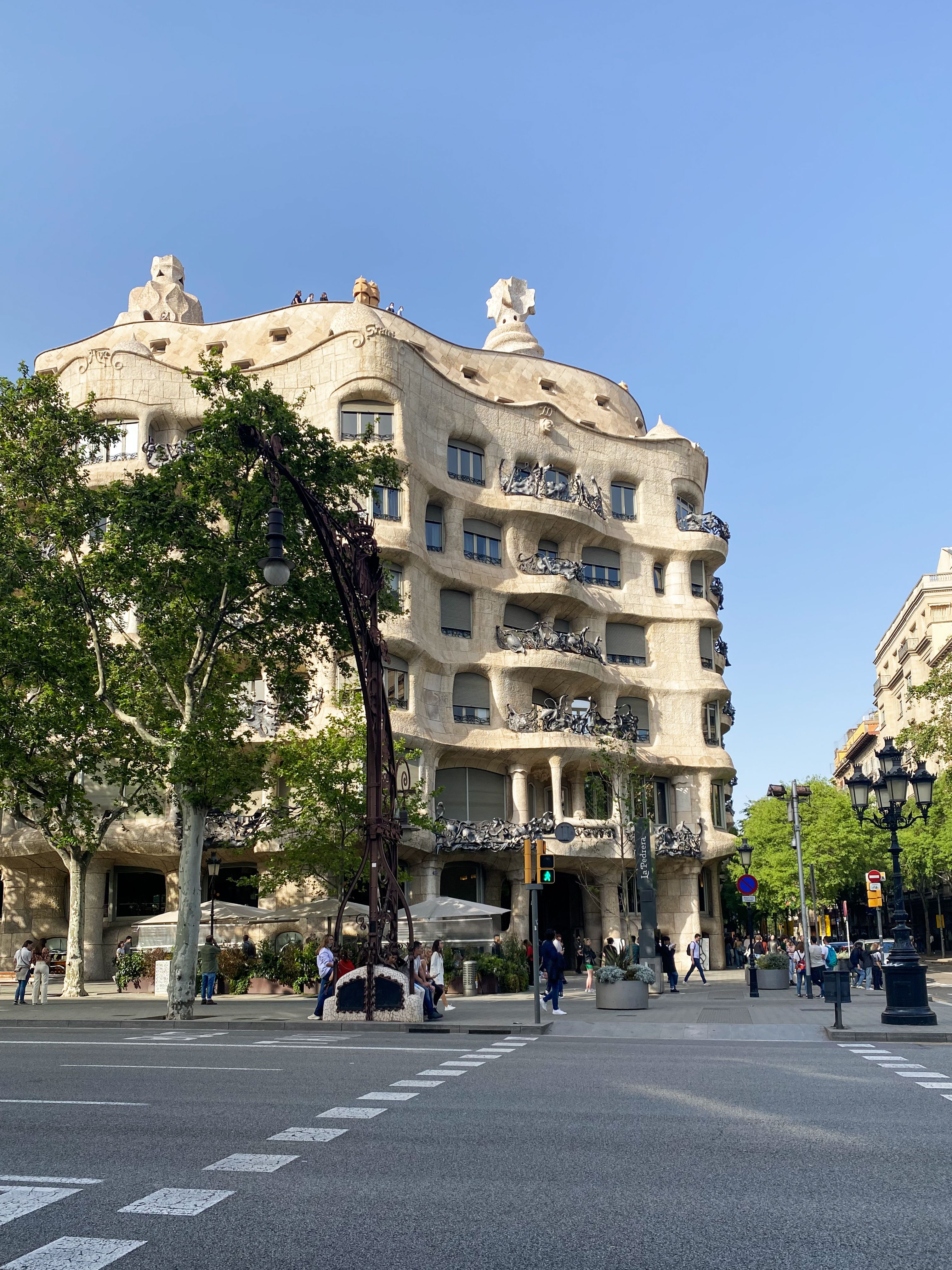 Photo of Casa Milà on a sunny day in Barcelona with people walking nearby.