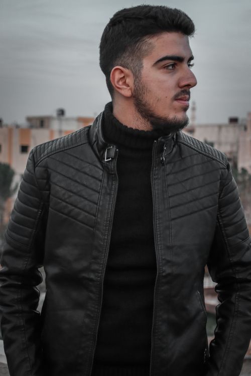 Free Portrait of a young man in a black leather jacket and turtleneck, looking away outdoors. Stock Photo