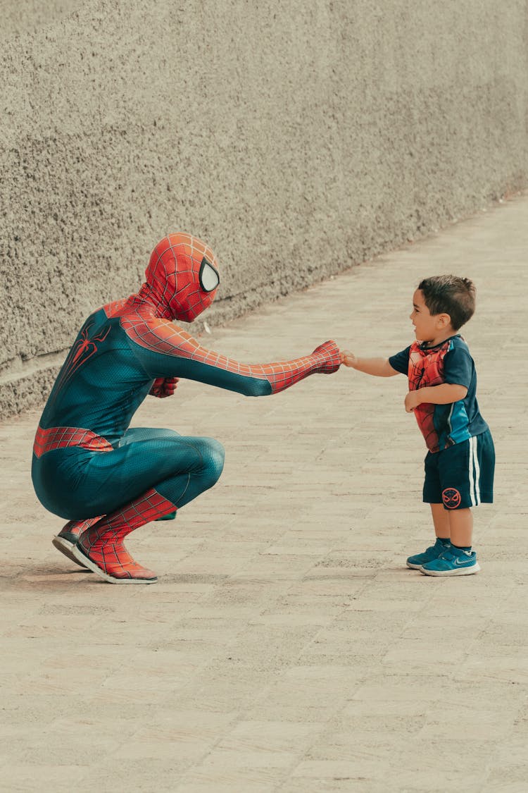 A Man In Spiderman Costume Doing Fist Bump On A Young Boy