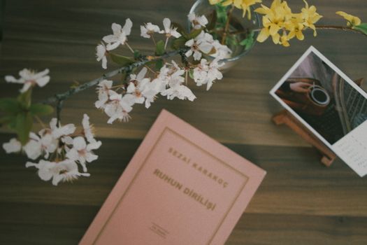Flat lay of a book with cherry blossoms and a photo on a wooden table, creating a serene and artistic composition.