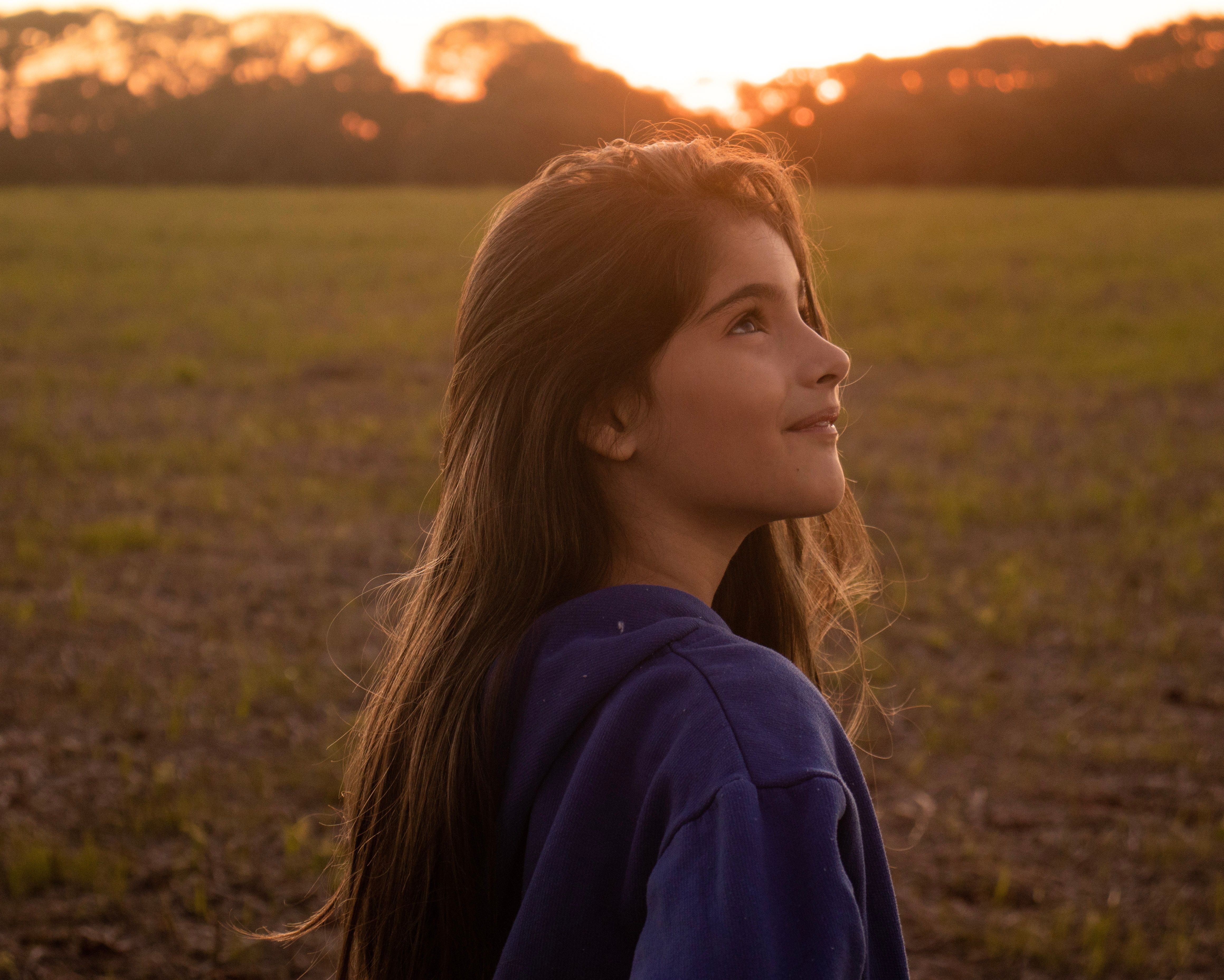 A Girl in Blue Hoodie Standing on Green Grass Field during Sunset ...