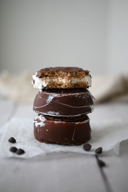 A stack of homemade choco pies showing the dark cocoa cake layers, white marshmallow filling, and glossy chocolate coating with one pie cut in half.
