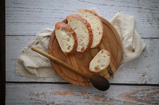 Top-down view of sliced artisan bread on a rustic wooden plate with a spoon and cloth.