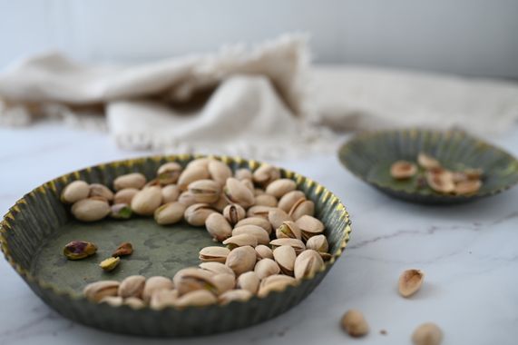 Pistaches em tigela verde rústica sobre superfície de mármore — apresentação para receita