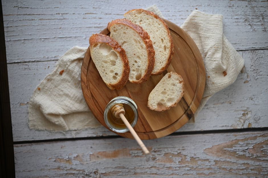 A golden loaf of bread machine white bread with several slices cut, showing an even, soft crumb, next to the bread machine pan it baked in.