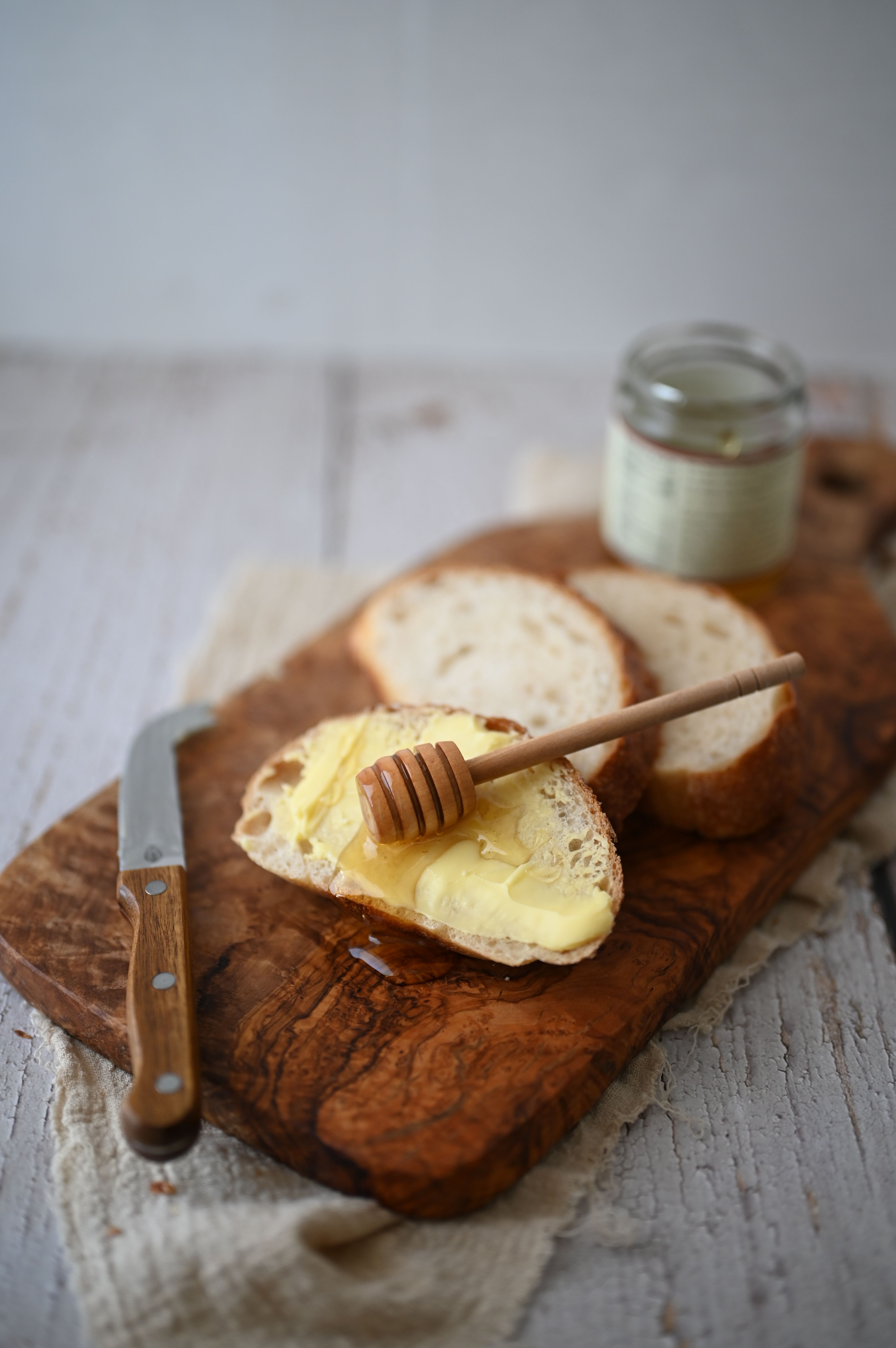 A rustic breakfast setup featuring sliced bread with butter and honey on a wooden board.