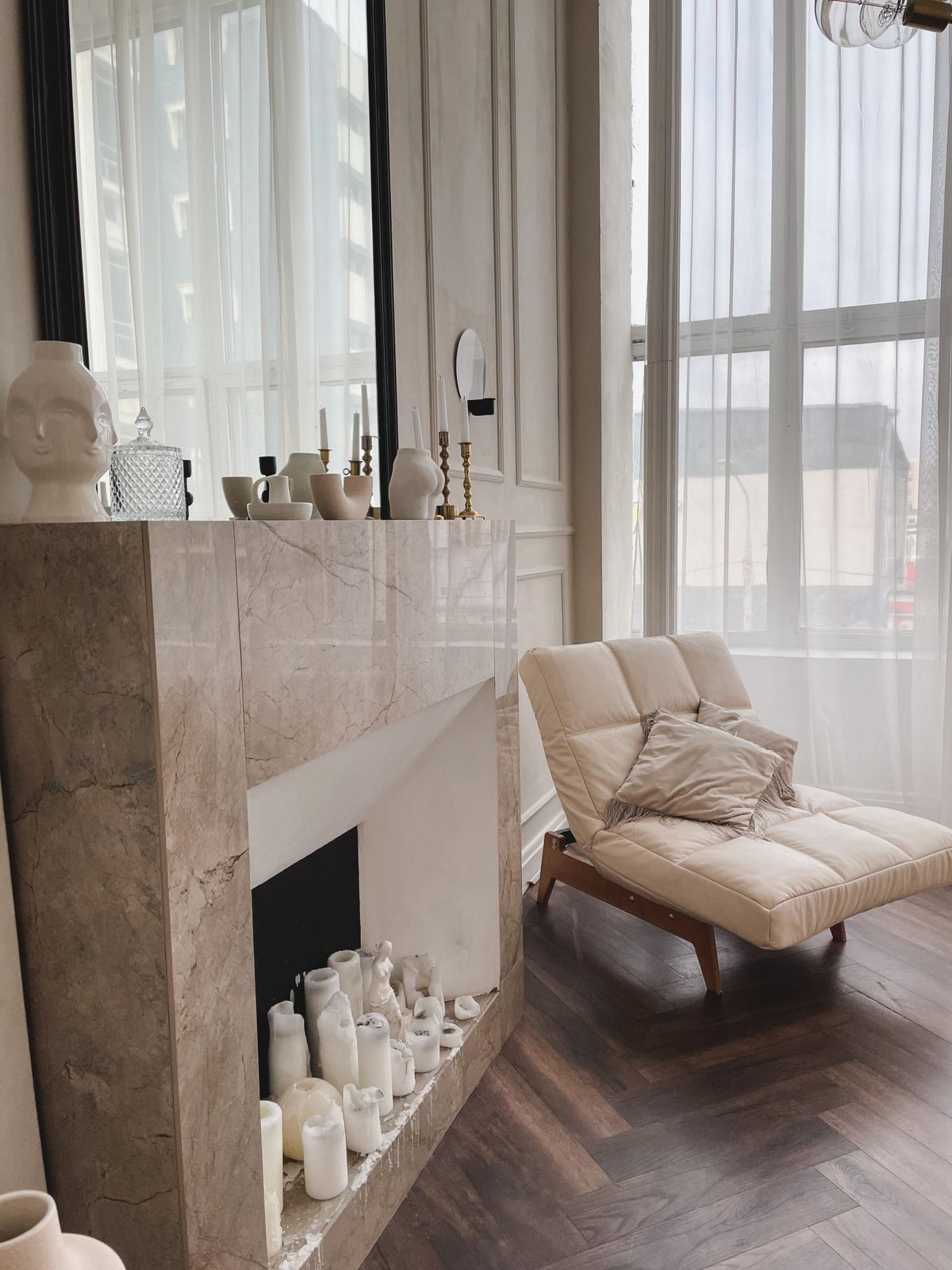 Elegant marble fireplace styled with candles beside a beige chaise in soft daylight