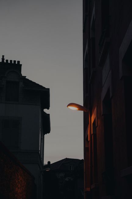 A dimly lit urban street scene captured at dusk, featuring a glowing street lamp.