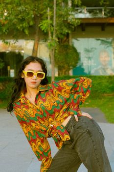 Woman in colorful retro outfit posing outside with sunglasses and hand on hip.