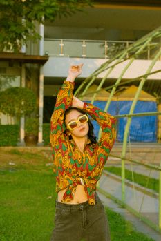 Young woman in vibrant retro shirt and sunglasses posing outdoors in natural light.