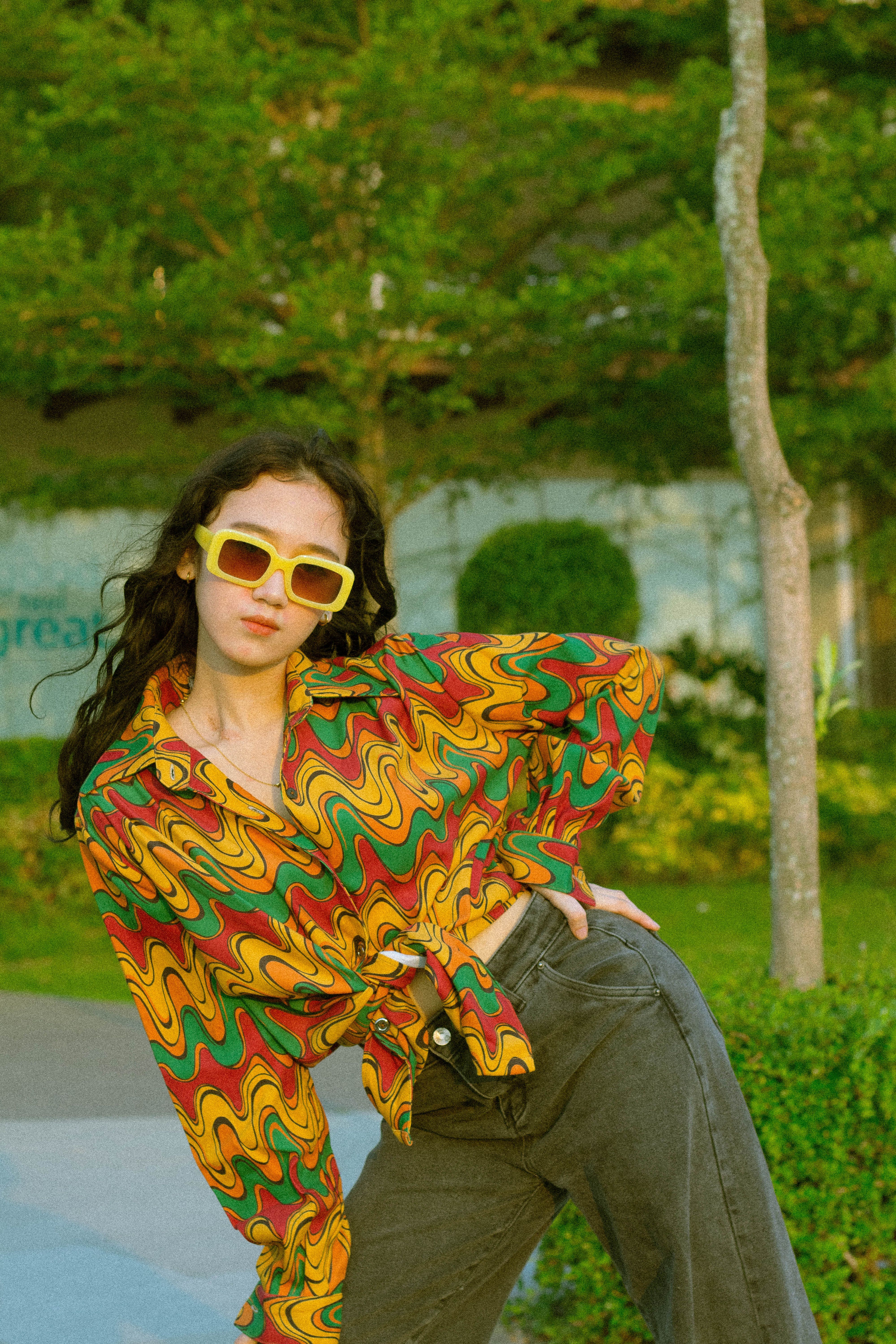 Fotomural Mujer a la moda posando al aire libre con una camisa retro colorida y gafas de sol.