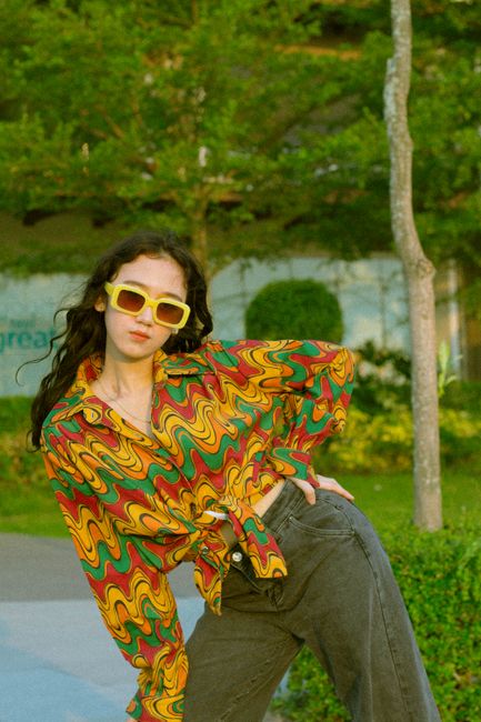 Fotomural Mujer a la moda posando al aire libre con una camisa retro colorida y gafas de sol.