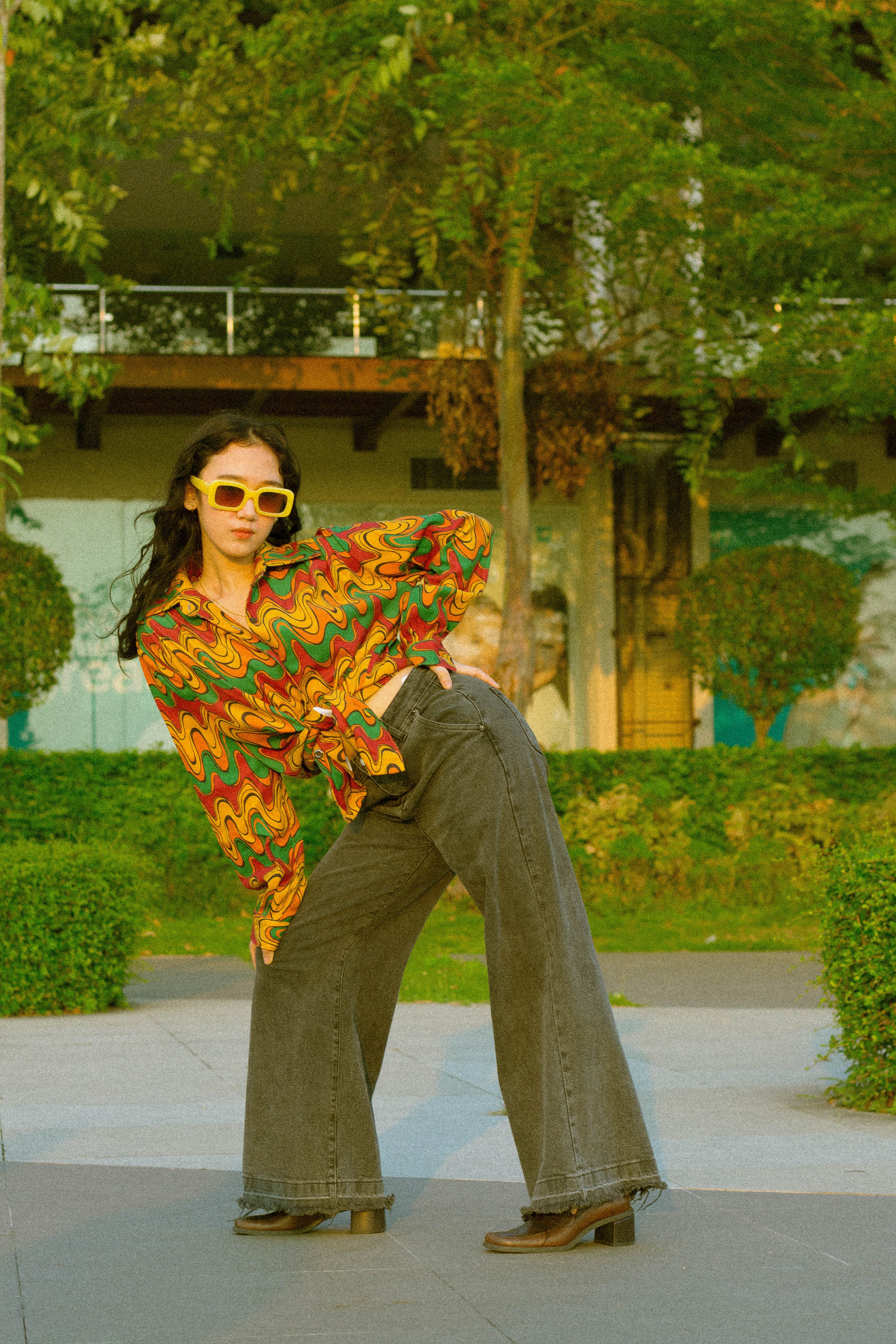 Fotomural Mujer a la moda con un atuendo colorido y gafas de sol posando al aire libre.