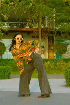 Fashionable woman in colorful outfit and sunglasses striking a pose outdoors.