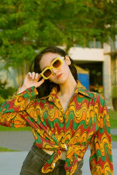 Young woman wearing sunglasses and a vibrant shirt posing outdoors in bright light.