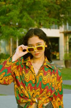 Confident young woman in vibrant outfit posing outdoors with trendy sunglasses.