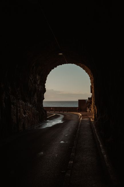A dark tunnel opens up to a scenic view of the sea and coastline.