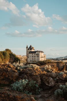 Explore this breathtaking view of a historic castle perched on a rocky hill, under a serene cloudy sky. by Mathilde Langevin