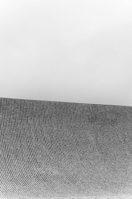 Minimalist black and white image of a textured wall creating a stark contrast against a blank sky.