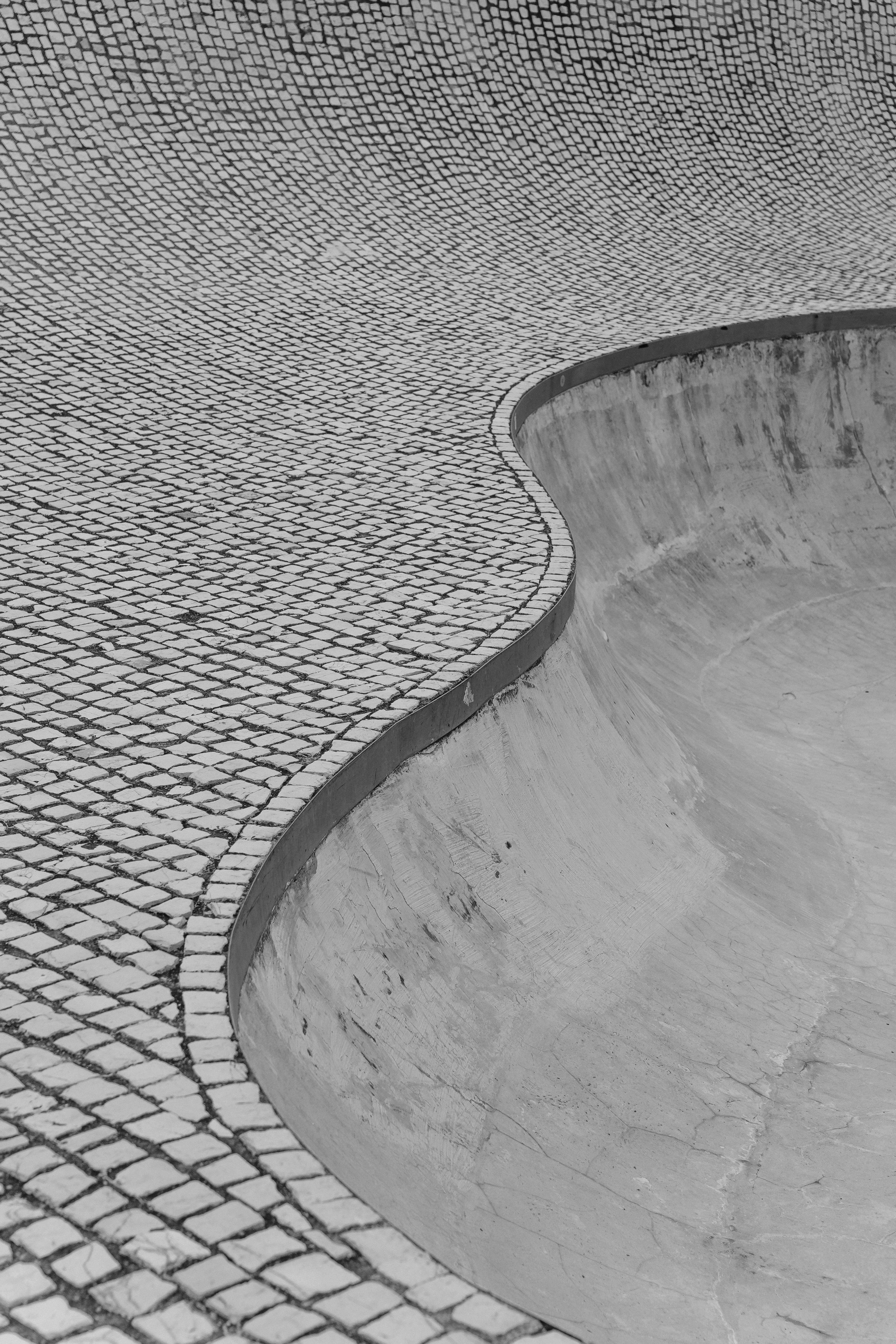 Artistic black and white photo capturing the curve of a skate park's tiled surface.