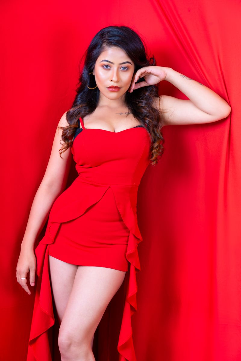 Elegant portrait of a woman posing confidently in a red dress against a red background.