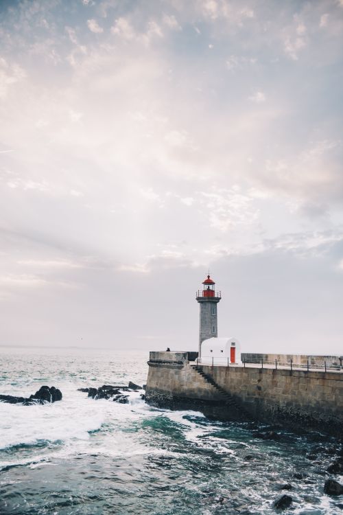 Free Felgueiras Lighthouse stands tall on a pier with waves crashing, under a serene sky in Porto, Portugal. Stock Photo
