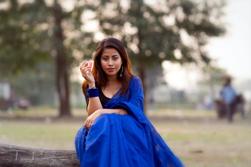 Beautiful woman in a blue dress poses elegantly outdoors, showcasing fashion and style.