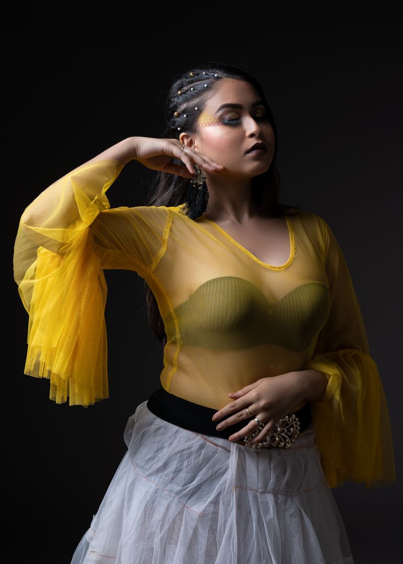 Model posing in stylish yellow outfit with dramatic lighting and elegance.