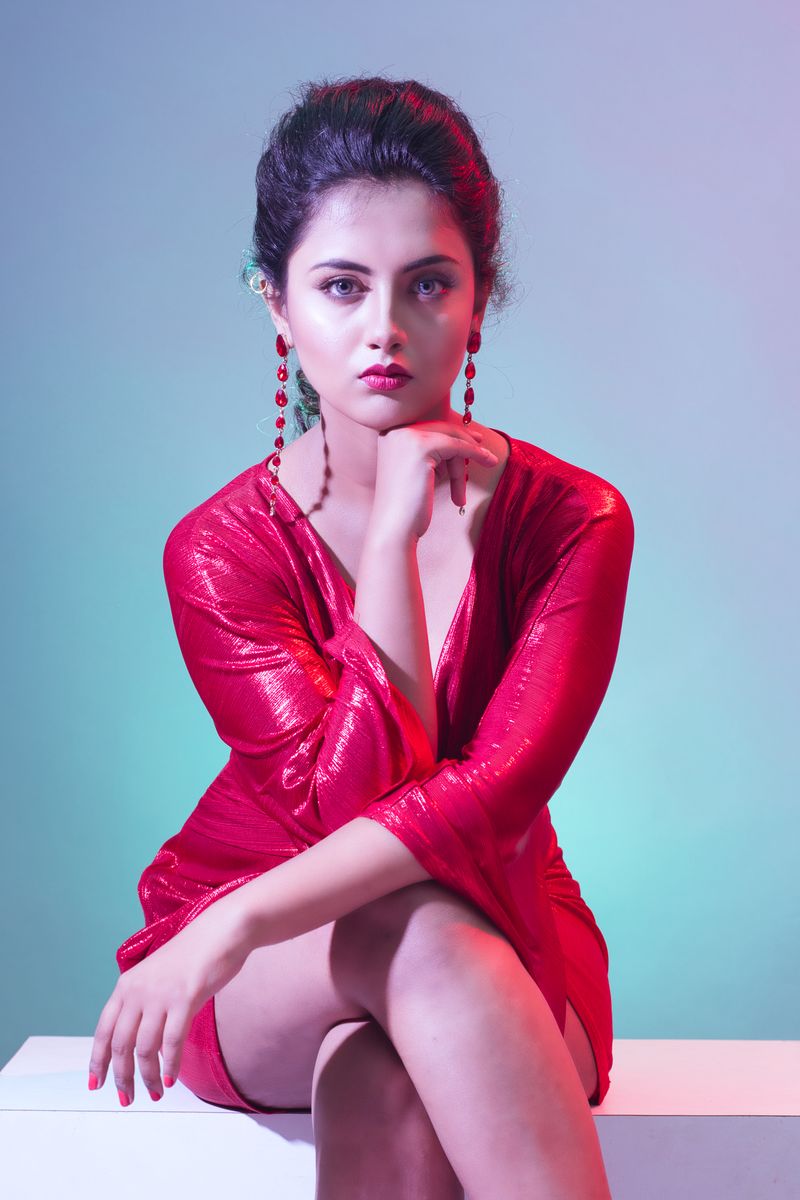 Stylish young woman in a red dress posing elegantly in a studio setting.