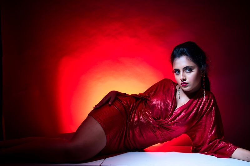 A stylish photoshoot of a woman in a shimmering red dress striking a pose under dramatic red lighting.