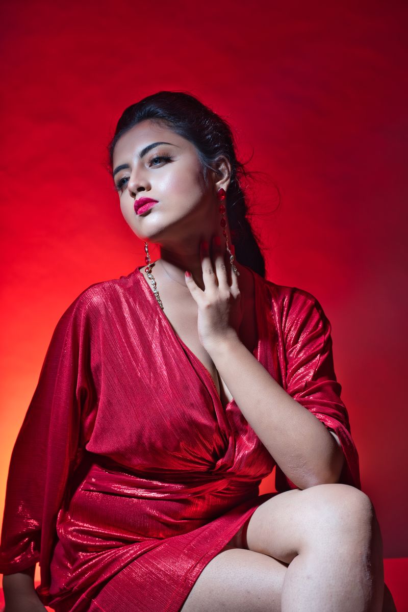 Striking portrait of a woman in a red dress with vibrant red background, posing elegantly.