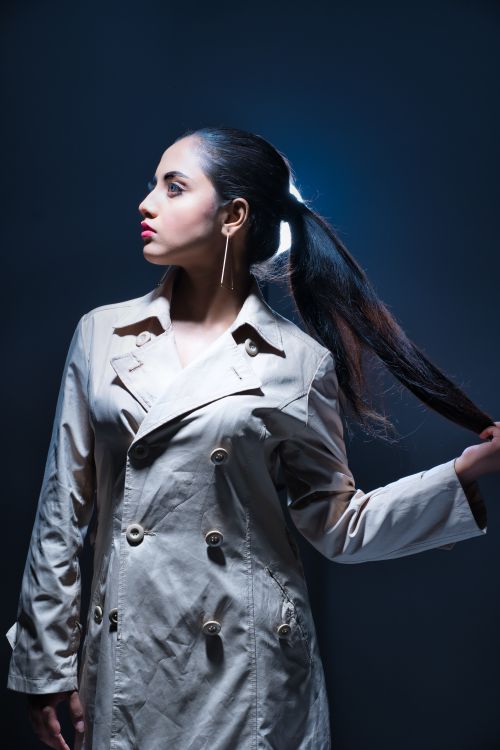 Free Elegant fashion portrait of a woman in a trench coat posing in dramatic lighting. Stock Photo